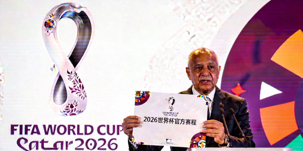 国际足联官员在新闻发布会上展示2026世界杯官方赛程文件，背景是巨大的赛事会徽